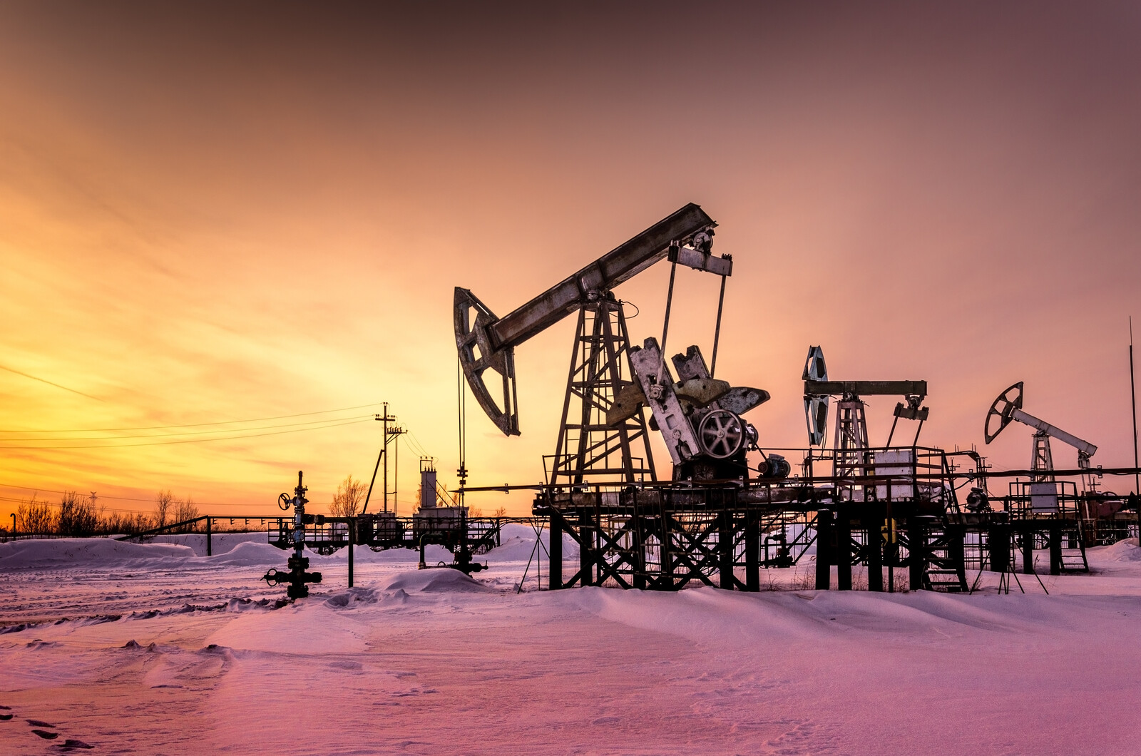 A pumpjack seen in winter during sunset.